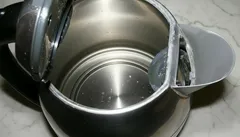 Binnenkant van een open elektrische waterkoker met wat water en kalkaanslag zichtbaar.